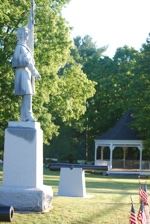 Image of soldier shaped monument in grass with pagoda in background
